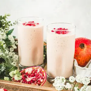 Pomegranate mango smoothies in glass cups with pomegranate seeds on top.