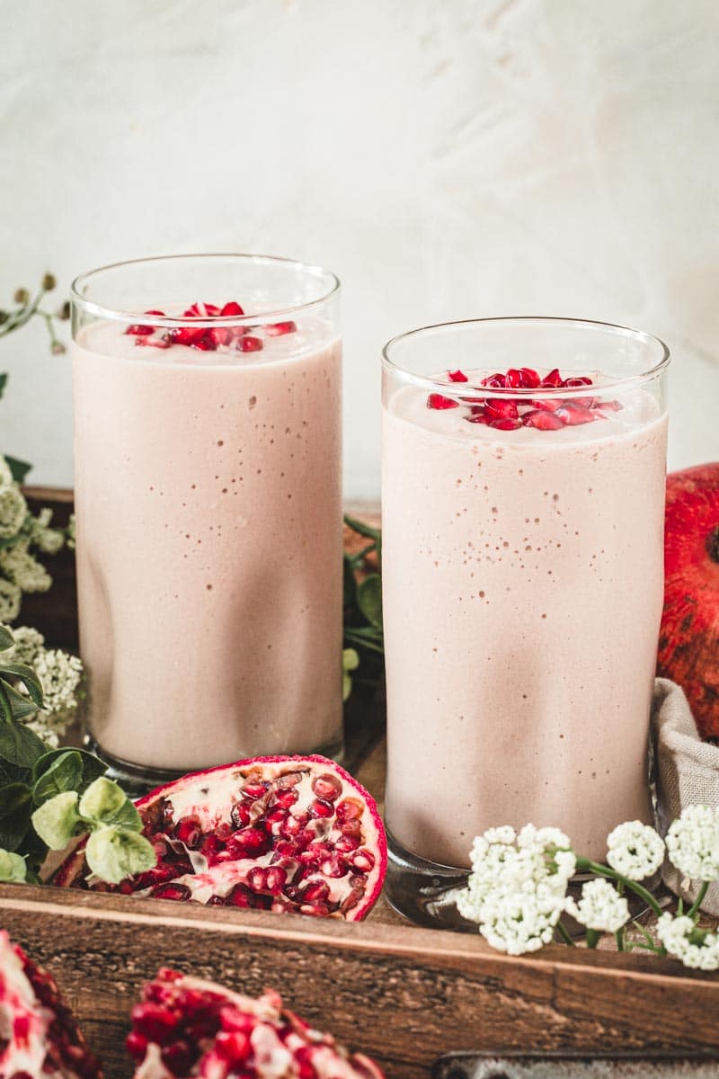 Two pomegranate mango smoothies topped with pomegranate seeds.
