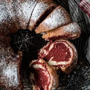 Red velvet marble bundt cake sliced and covered in powdered sugar.