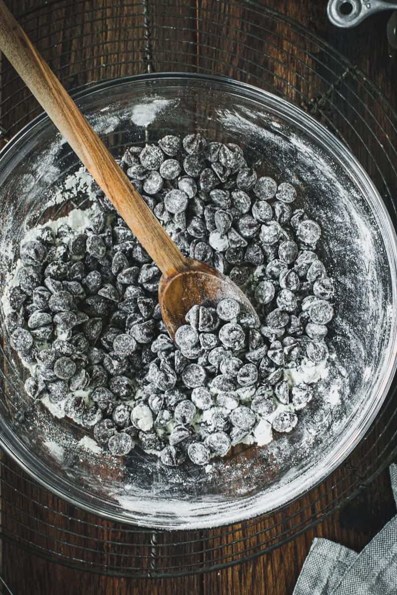 Chocolate chips covered in flour in a glass mixing bowl on a round wire rack.
