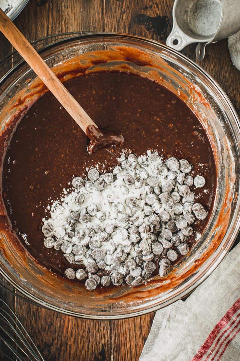 Chocolate chips covered in flour on top of brownie batter in glass mixing bowl.
