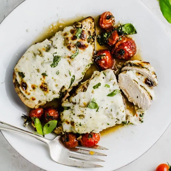 Balsamic baked chicken in a white plate with silver serving fork.