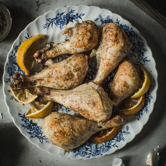 Chicken drumsticks with roasted lemon wedges on a blue and white floral plate.
