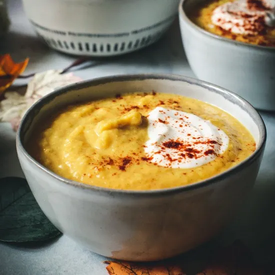 Acorn squash soup topped with sour cream and paprika in a small gray bowl.