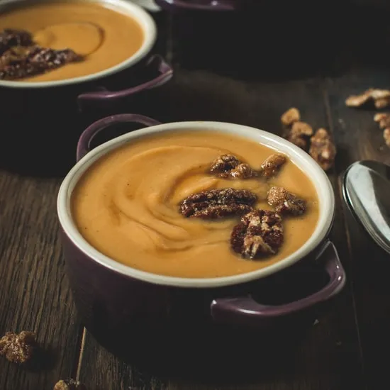 Maple sweet potato soup topped with candied pecans in a small purple bowl.