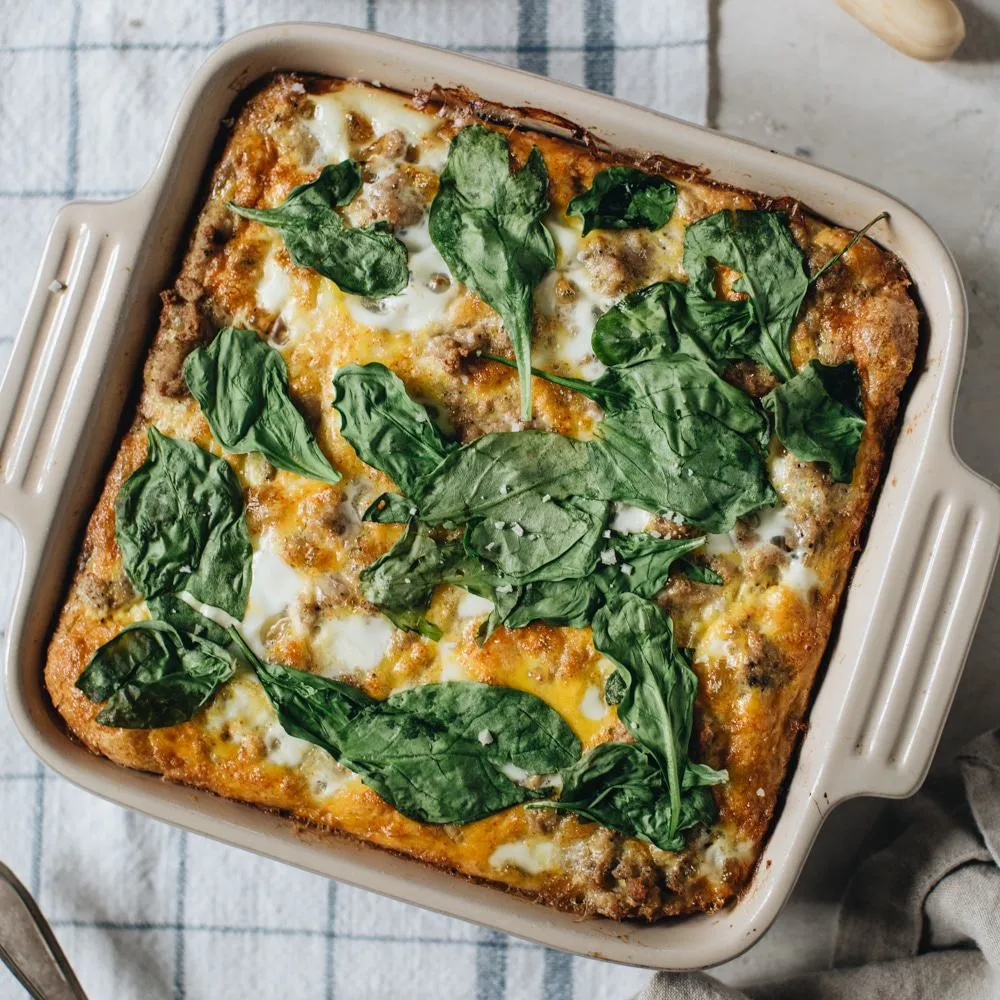 Turkey and egg breakfast casserole topped with spinach leaves in a square baking dish.