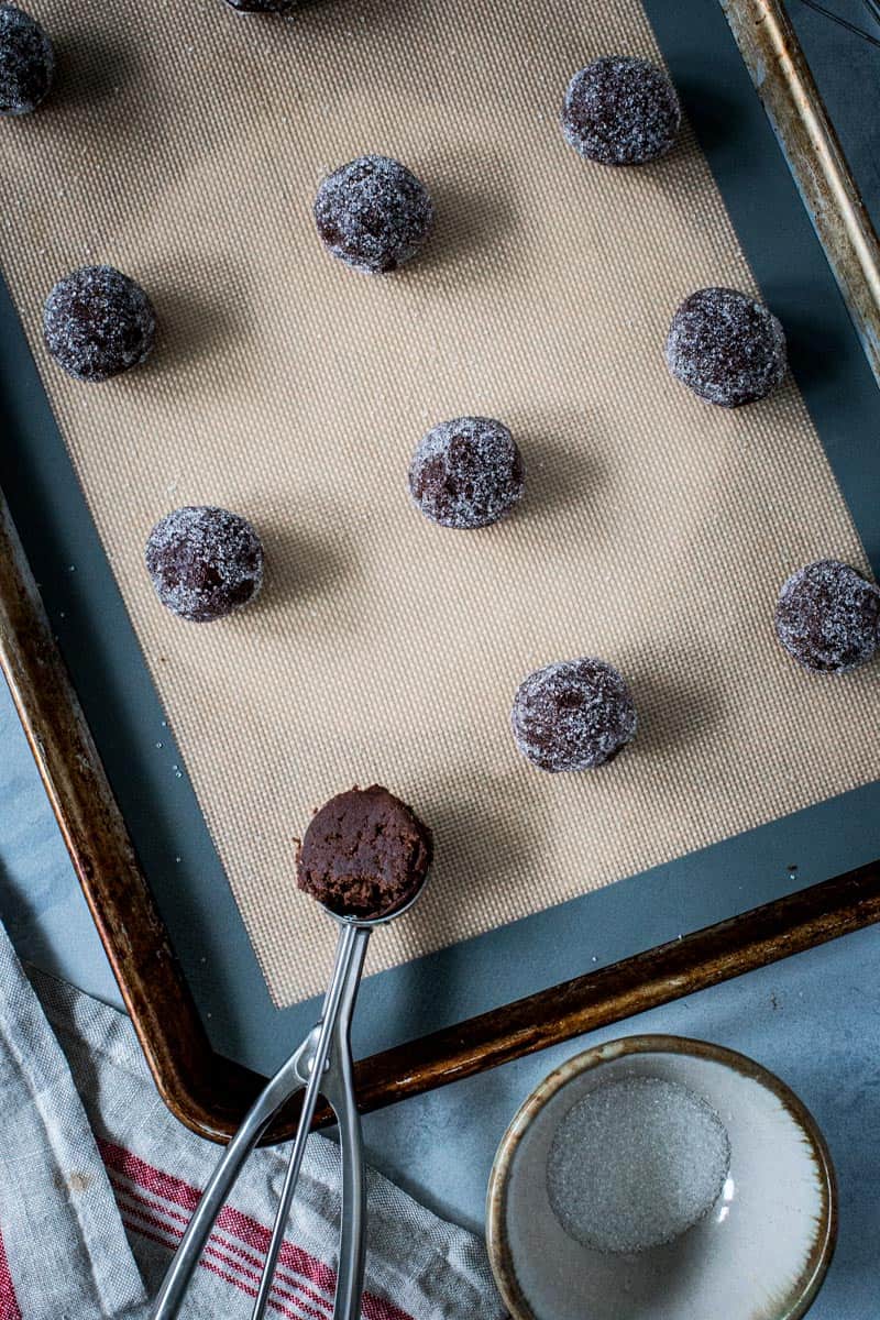 Ginger cookie dough balls rolled in sugar on a baking sheet.