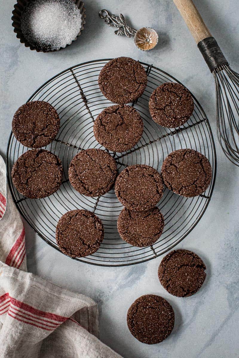 Chocolate ginger cookies on a round wire rack with red and cream towel next to it.