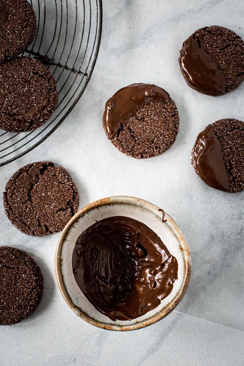 Melted chocolate in pottery bowl with ginger cookies half dipped sitting next to it.