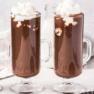 Two homemade hot chocolates in tall slim mugs topped with whipped cream.