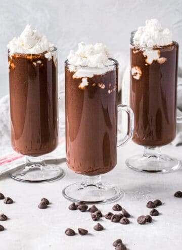 Three homemade hot chocolates topped with whipped cream in tall slim glasses.