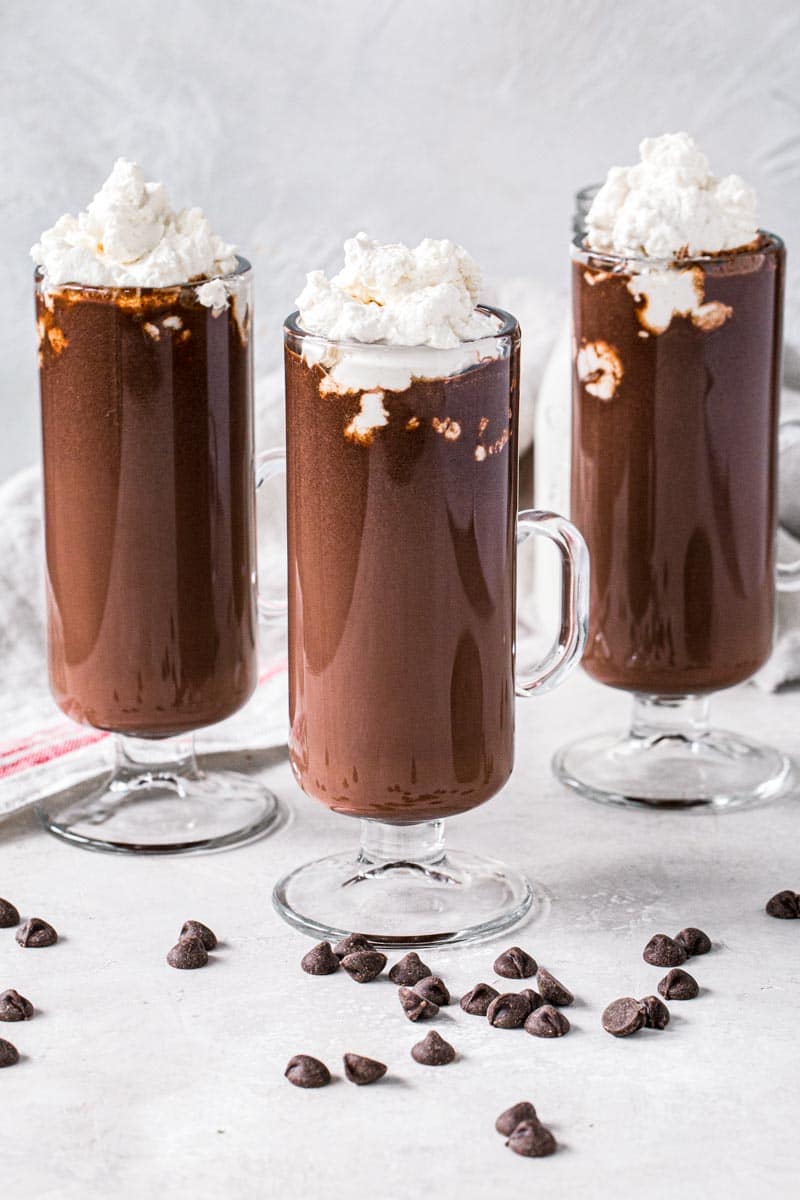 Three homemade hot chocolates topped with whipped cream in tall slim glasses.