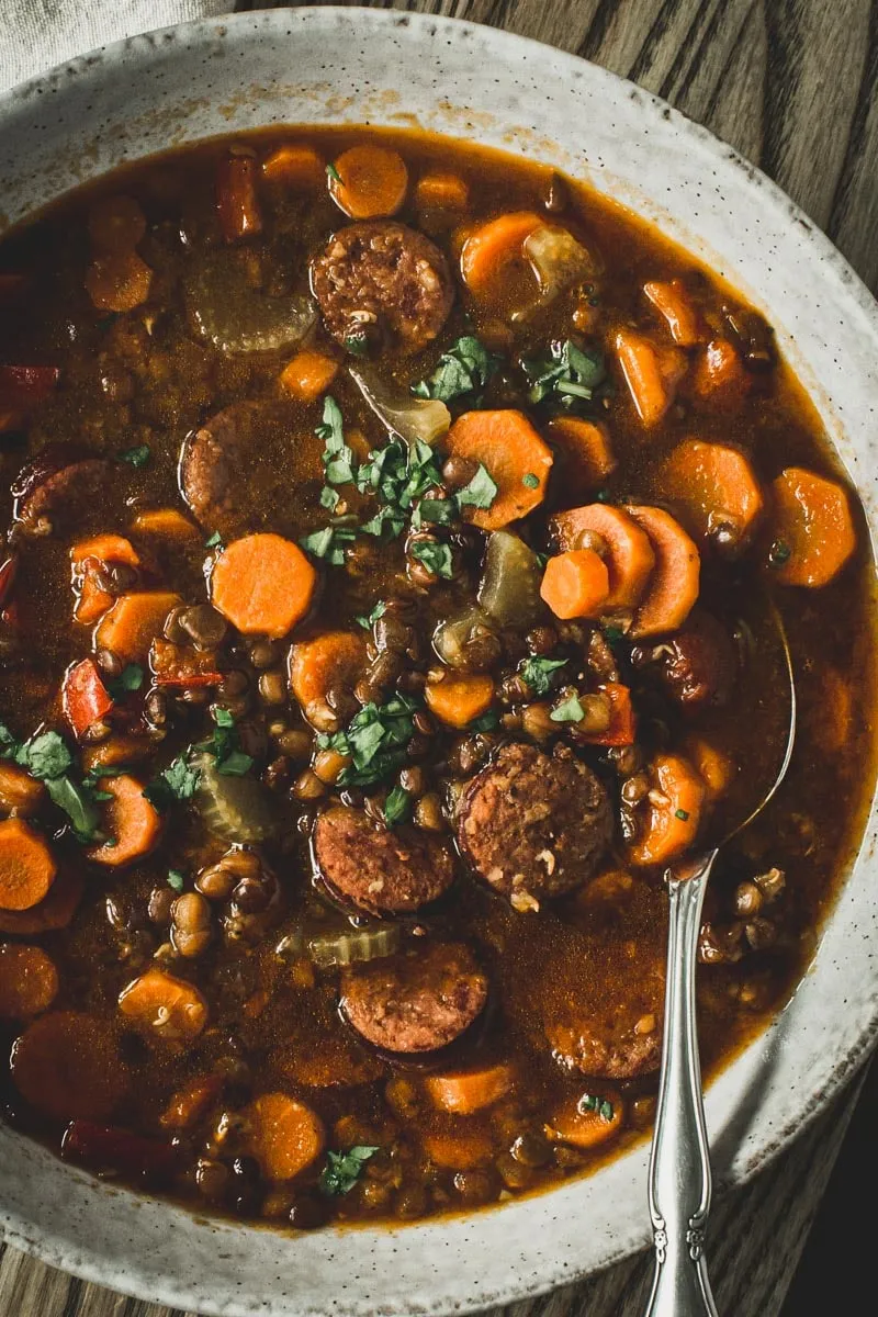 Silver spoon in sausage and lentil stew in a white bowl.