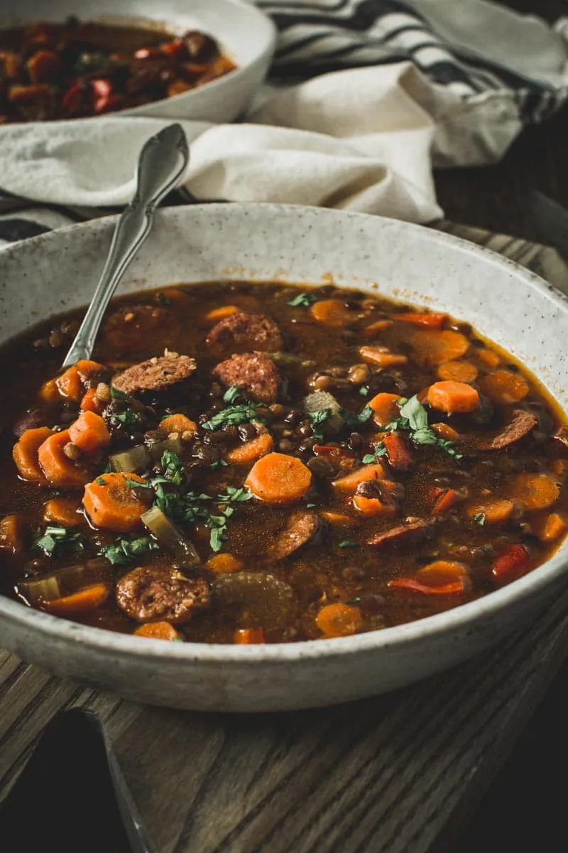 Sausage and lentil stew with a silver spoon in a white bowl.