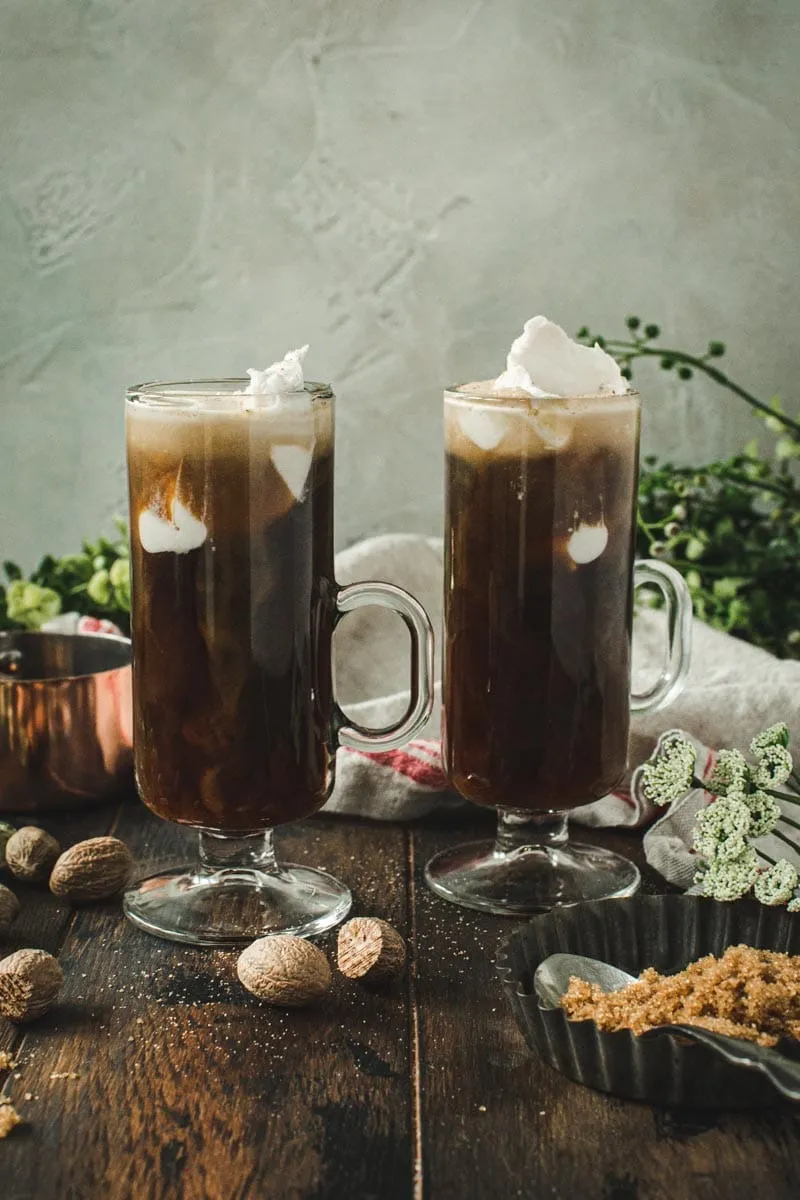 Two Irish coffees with coconut milk sprinkled with nutmeg and in tall slim mugs.