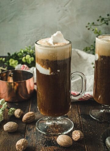 Tall slim glass filled with vegan Irish coffee with coconut cream on top.
