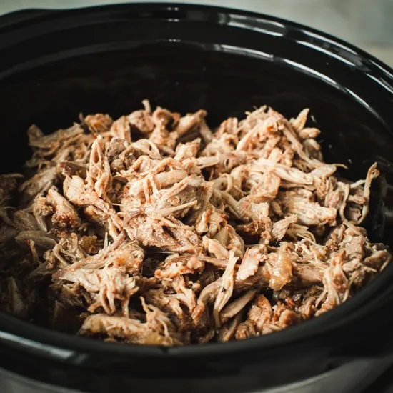 Pulled pork sitting a black rimmed slow cooker.