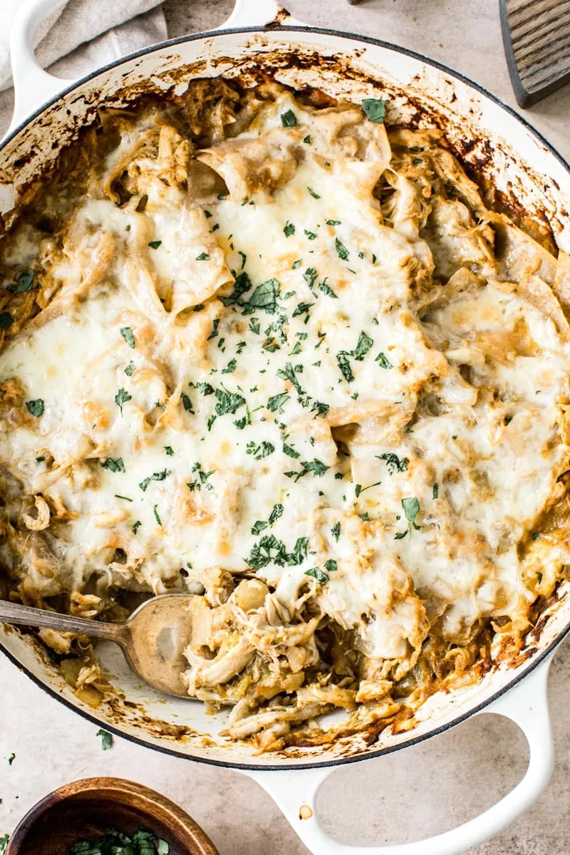 Silver serving spoon in chicken enchilada skillet topped with fresh cilantro.