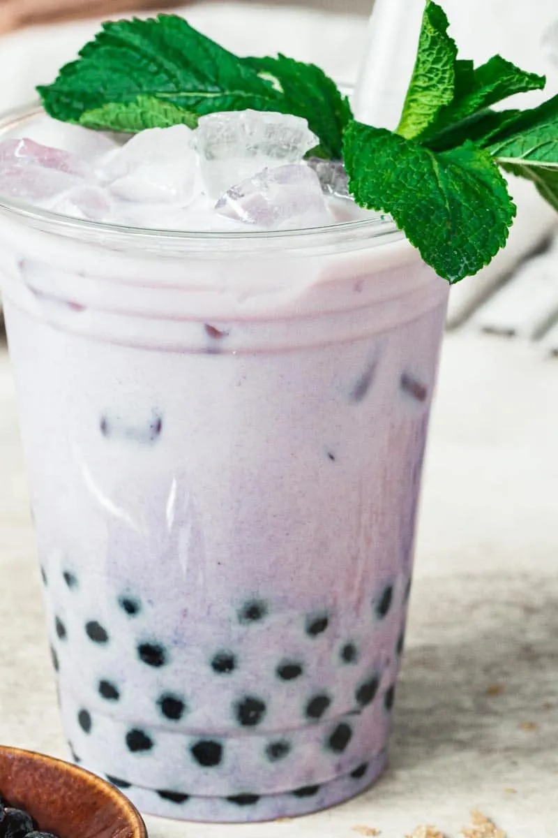 Close up of taro bubble tea in a plastic cup with mint leaves on top.