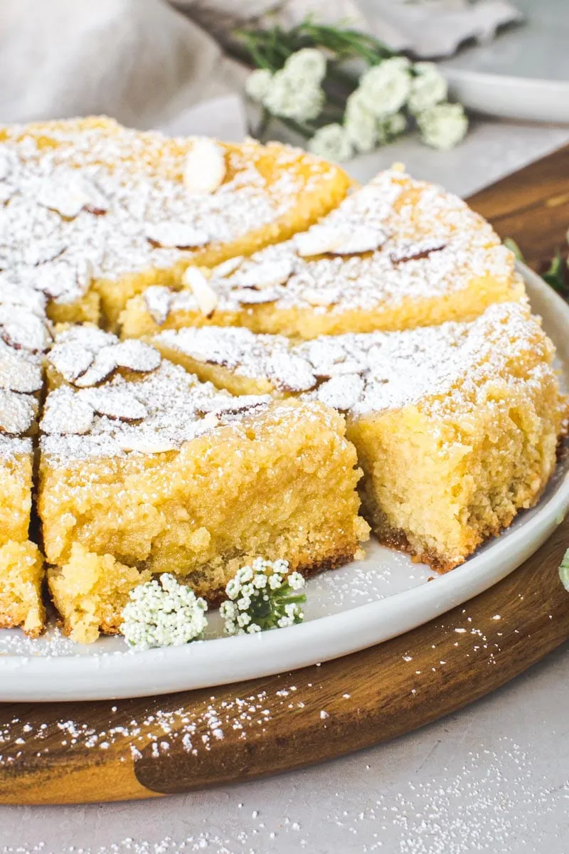 Slices of lemon ricotta cake on a white plate sitting on top of a wooden cutting board.