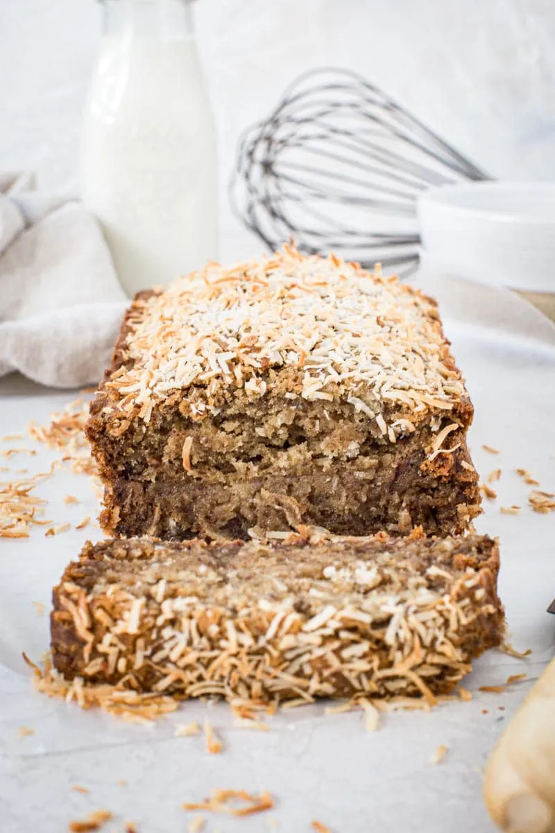 Loaf of vegan banana bread with a slice cut off and sitting on wax paper.