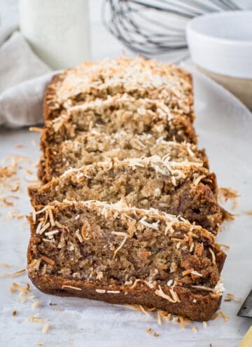 Slices of vegan banana bread topped with toasted coconut on wax paper.