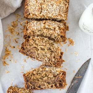 Slices cut off vegan banana bread with a wooden handled knife laying next to it.