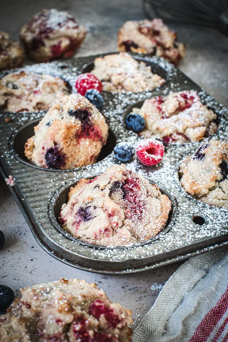 Powdered sugar covering a tin filled with mixed berry cornbread muffins.