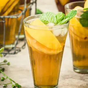 Tall glass of sangria iced tea filled with peaches and lemon and topped with mint.