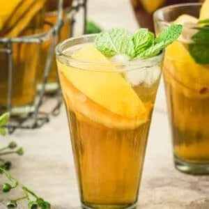 Tall glass of sangria iced tea filled with peaches and lemon and topped with mint.