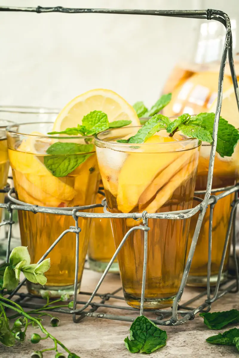 Mint topped sangria iced tea in glasses sitting in a metal drink carrier.
