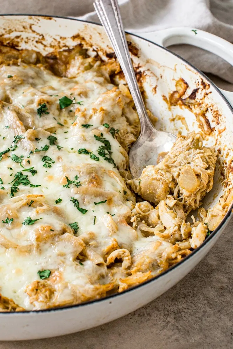 Silver serving spoon scooping into green chicken enchilada skillet topped with fresh cilantro.