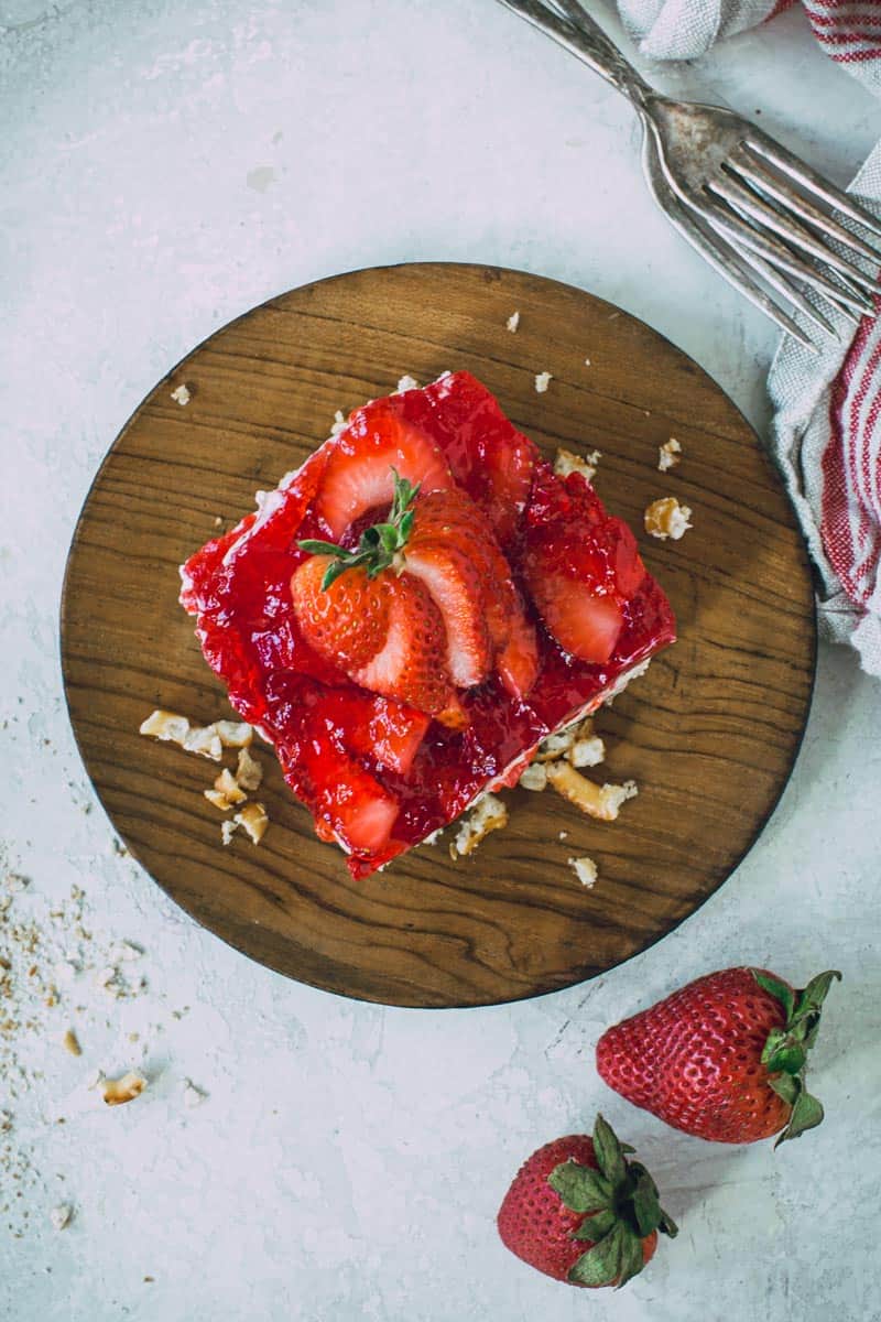 Sliced strawberry on top of strawberry pretzel salad on a wooden plate.