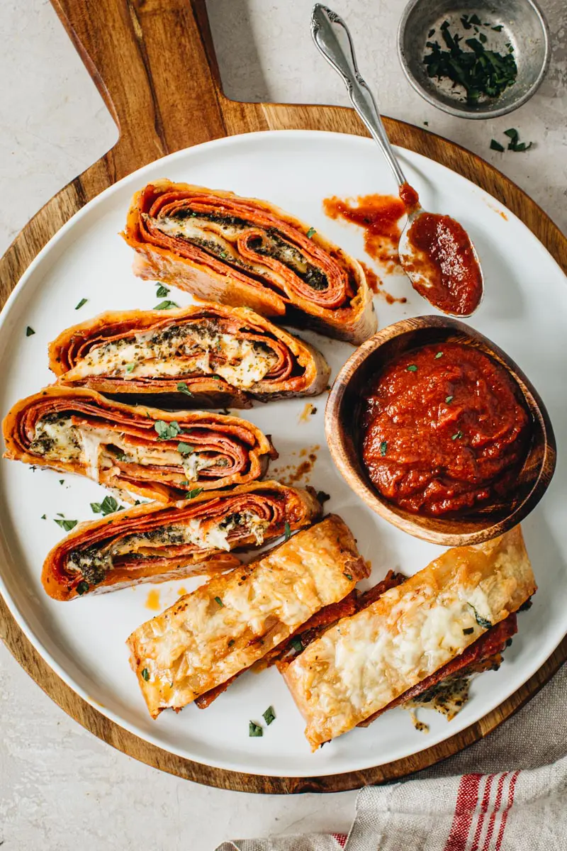 Slices on a round white plate with pizza sauce in a wooden bowl next to it.