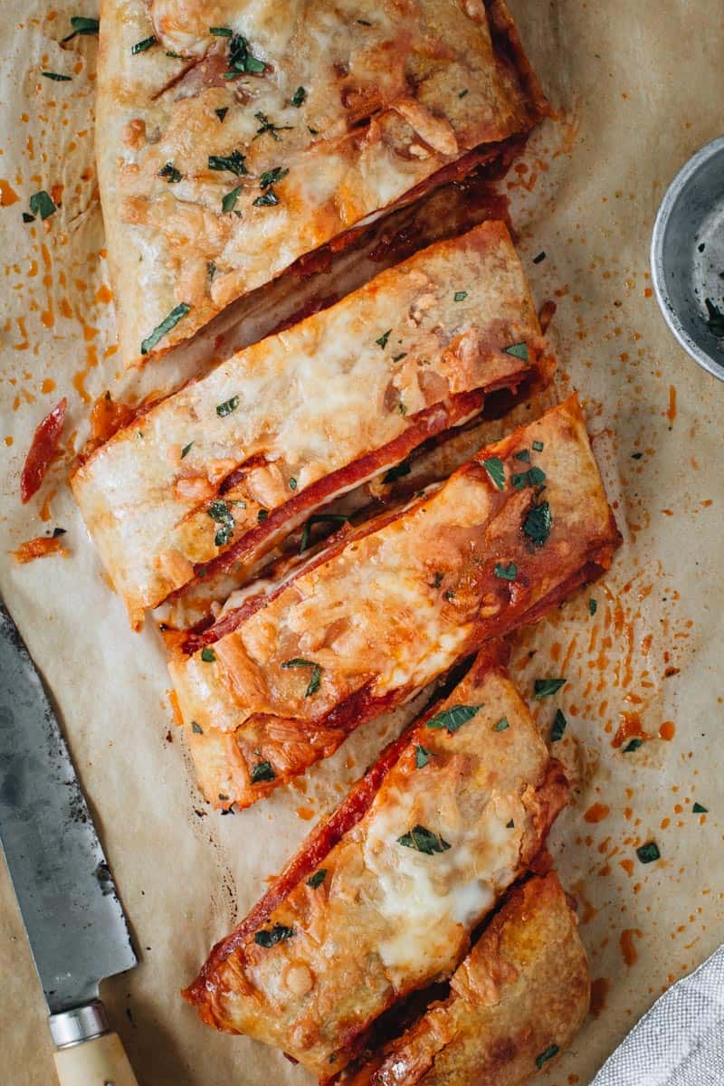 Stromboli half sliced and covered in melted cheese and fresh parsley.