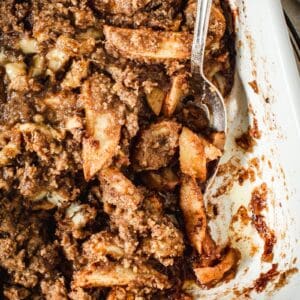 Apple banana crumble in a baking dish with a silver serving spoon.