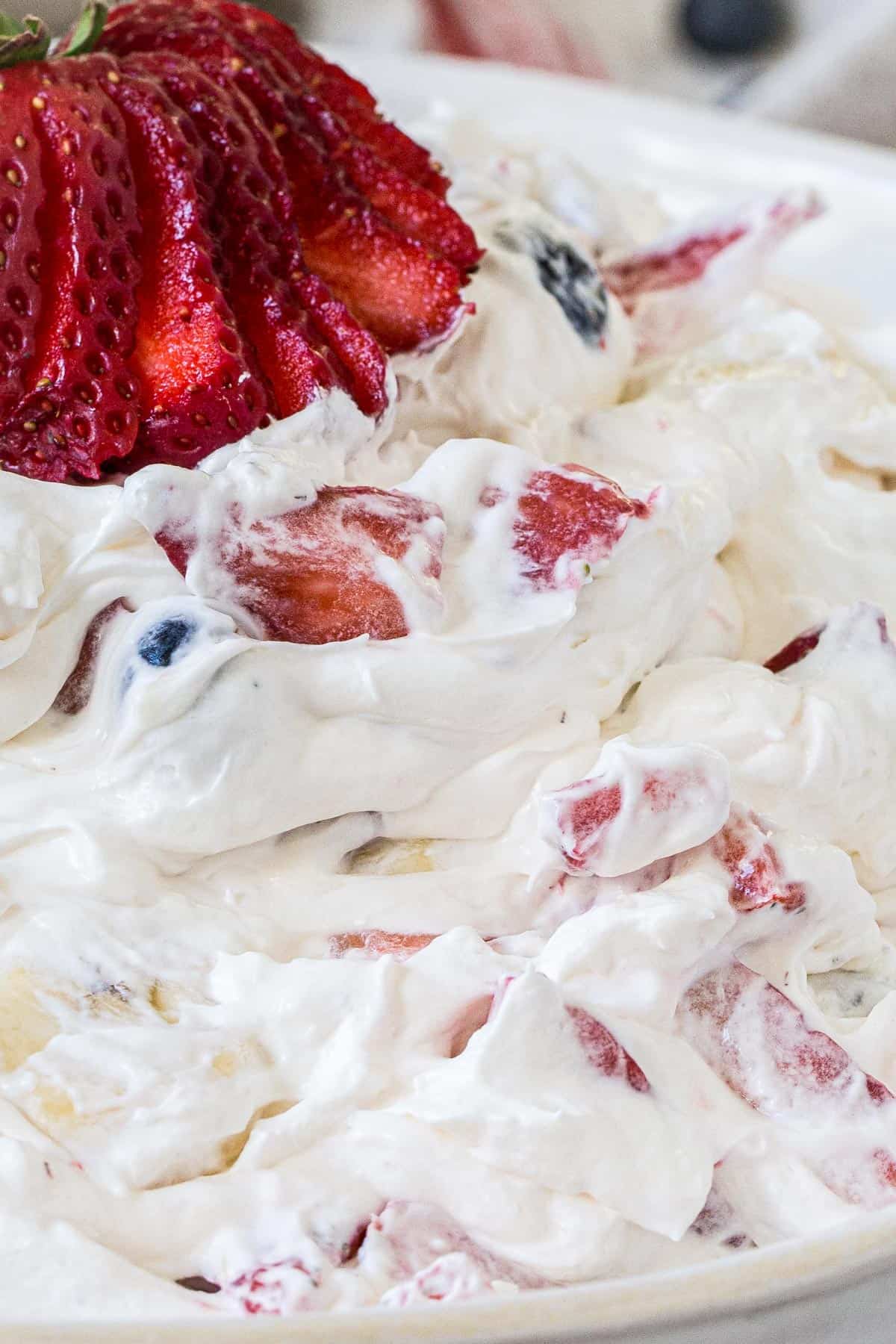 Sliced strawberry on top of red white and blue cheesecake salad.