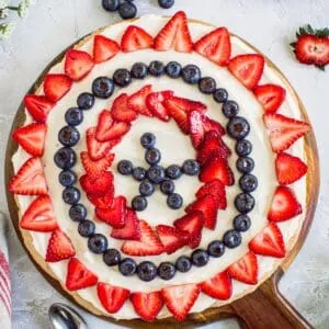 Fourth of July fruit pizza on a round wooden cutting board.