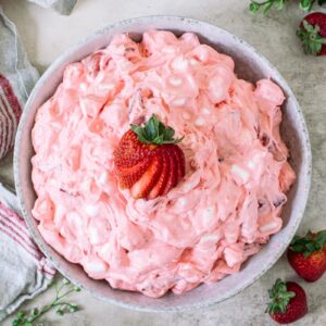 Strawberry jello fluffy salad topped with sliced strawberries in a round bowl.