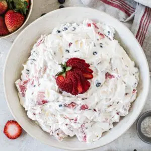 Red white and blue cheesecake salad with sliced strawberries and a bowl of strawberries beside it.