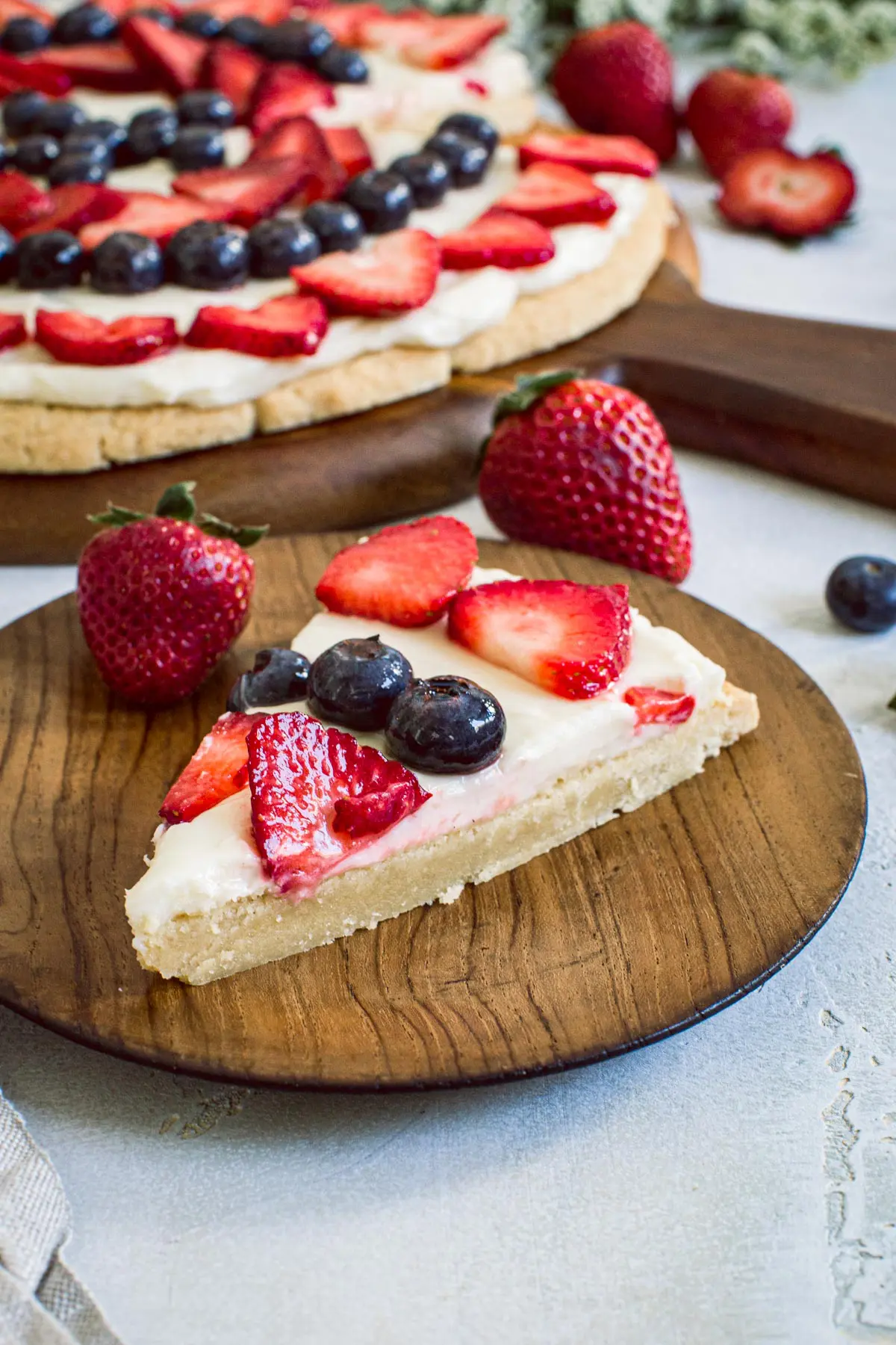 Slice of fruit pizza with strawberries and blueberries on a wooden plate.