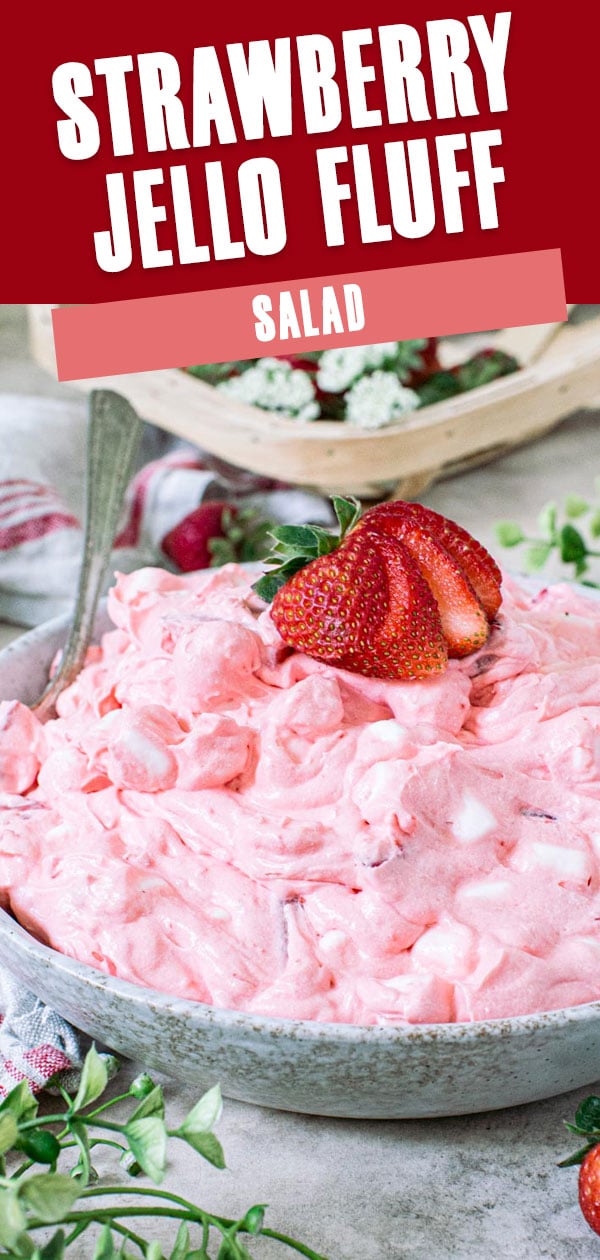 Strawberry Jello fluff salad topped with a sliced strawberry in a pottery bowl with silver serving spoon.