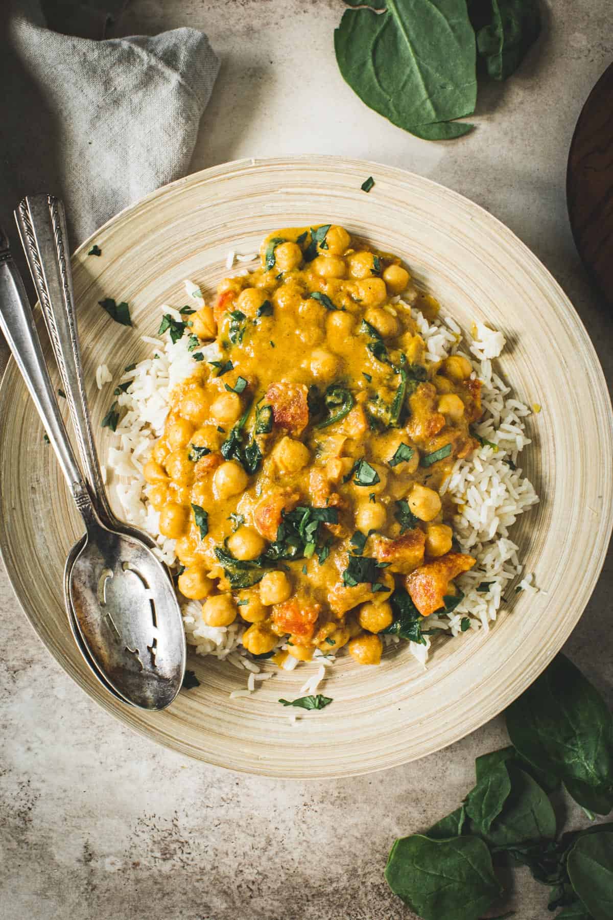 Vegan chickpea spinach curry on a bamboo plate with silver serving spoons.