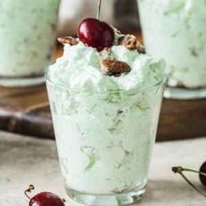 Pistachio pudding salad in a glass and topped with a cherry.
