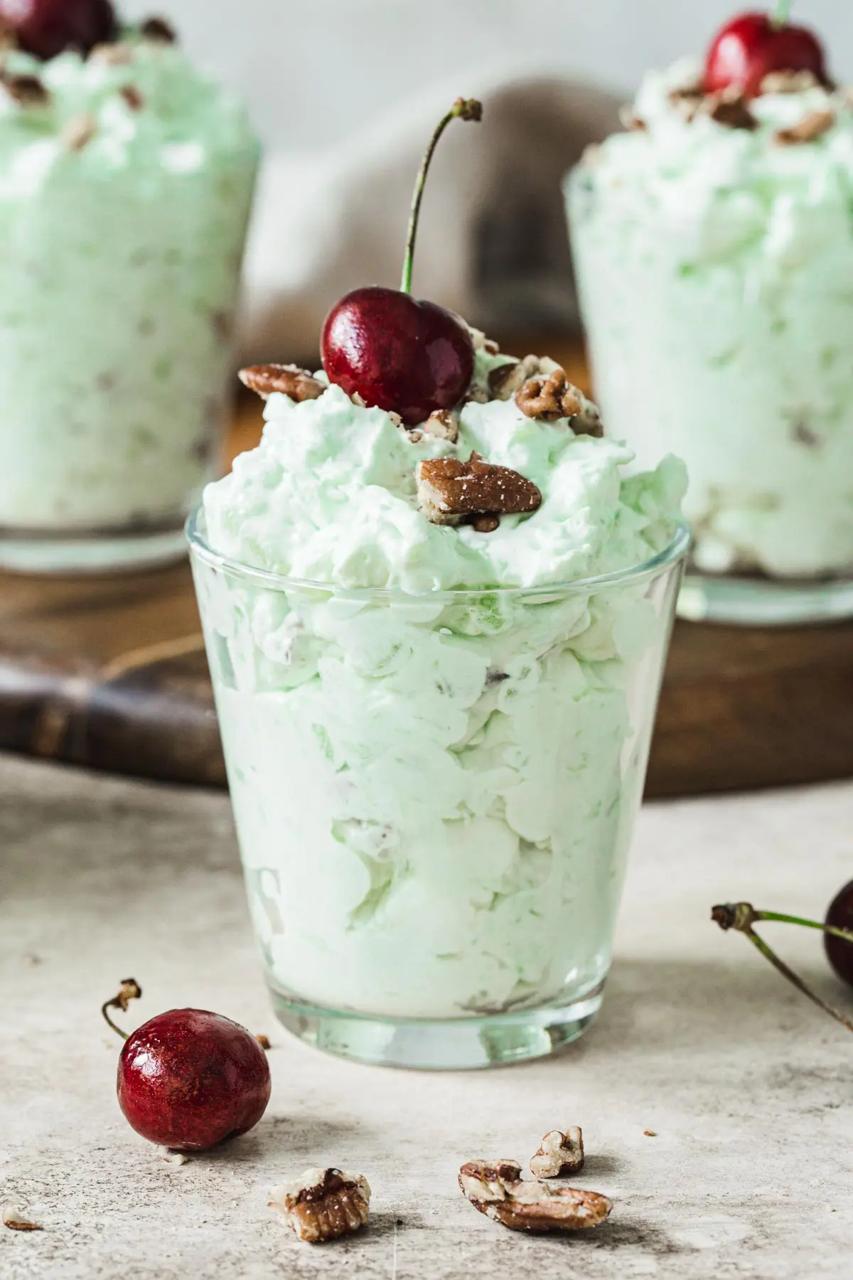 Pistachio pudding salad in a glass and topped with a cherry.