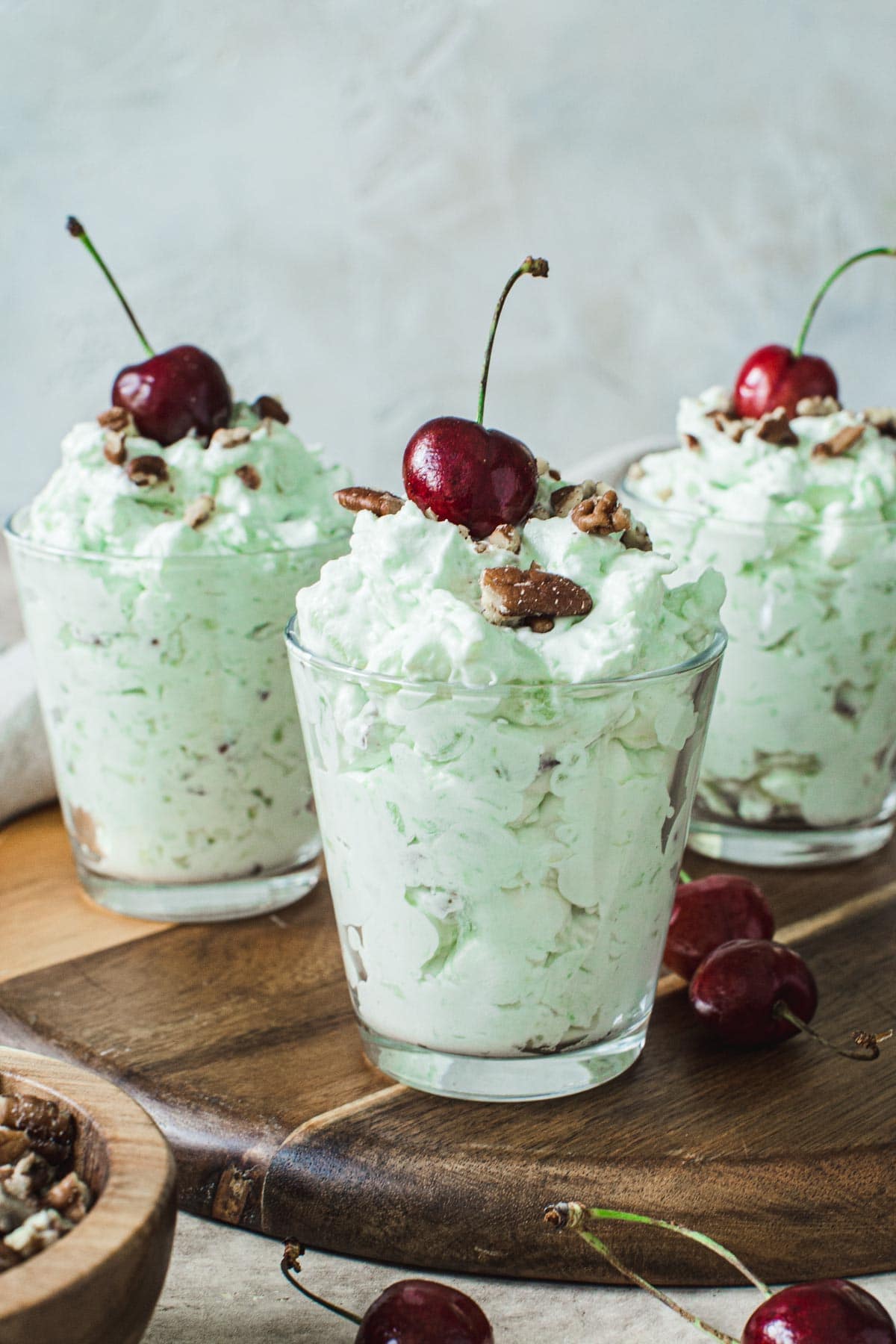 Watergate salad in glasses topped with cherries.