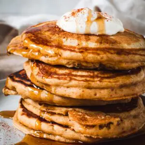 Sweet potato pancakes stacked and covered in maple syrup and topped with whipped cream.