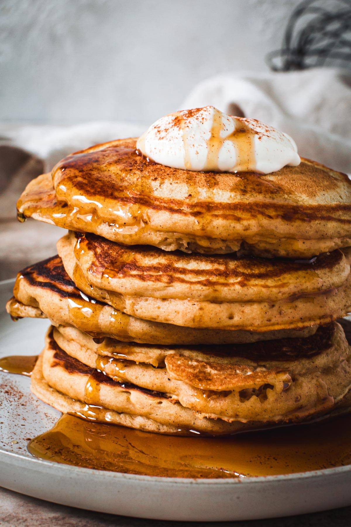 Sweet potato pancakes stacked and covered in maple syrup and topped with whipped cream.