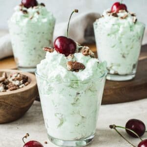Three glasses with watergate salad topped with cherries.