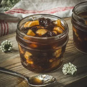 Dutch apple jam in a glass jar with a silver spoon next to it on a wooden board.